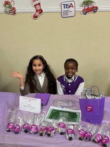 Two TISA girls presenting their handmade products at a school stall