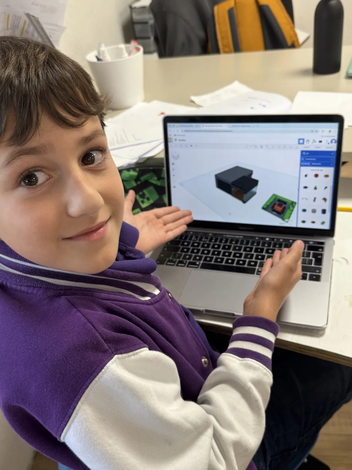 TISA student in a purple varsity jacket presenting his 3D CAD design on a laptop