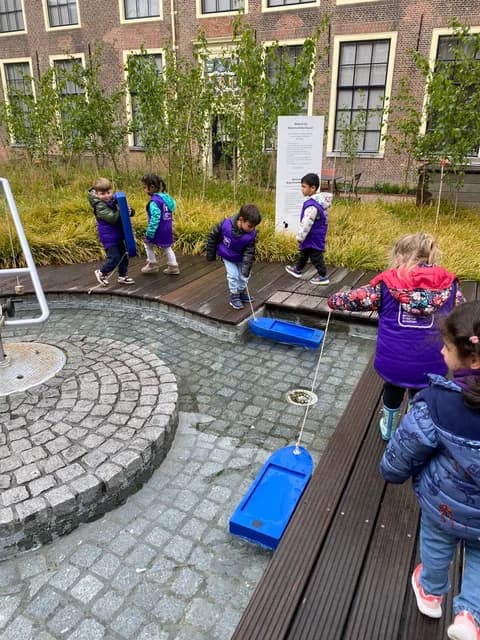 Students sailing toy boats along the courtyard water channel during a science lab