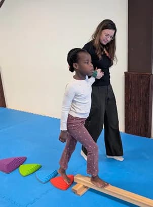 A TISA Care specialist guiding a young student on a balance beam in the gym
