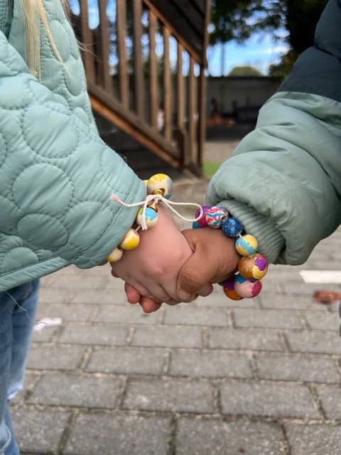 Two young children holding hands wearing colorful handmade bracelets in the courtyard