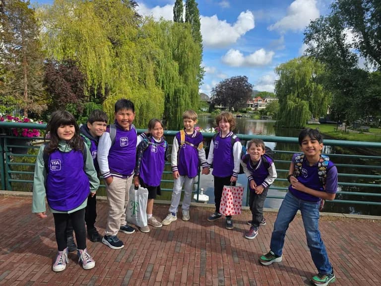 Eight TISA students in purple vests posing happily on a canal bridge near the Leiden campus