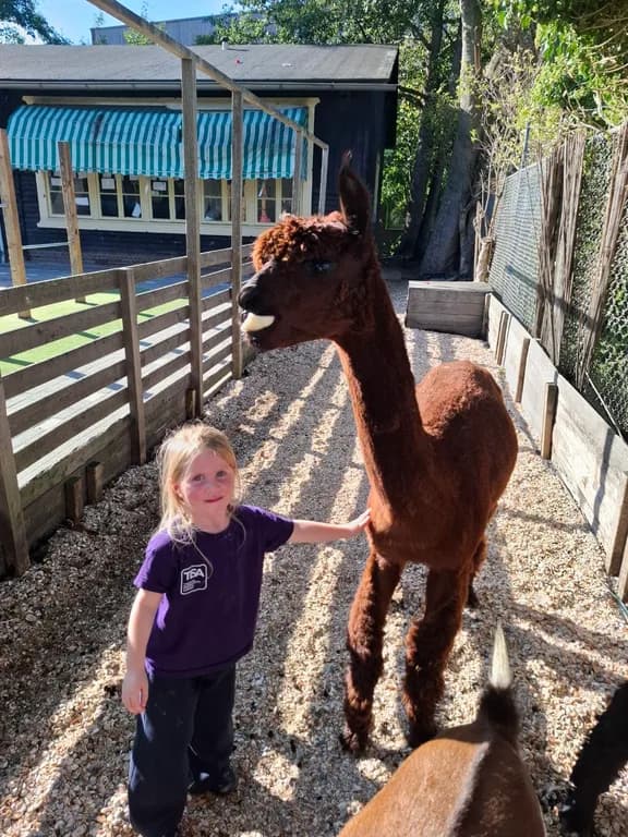 A young TISA student gently petting a baby animal at the school farm