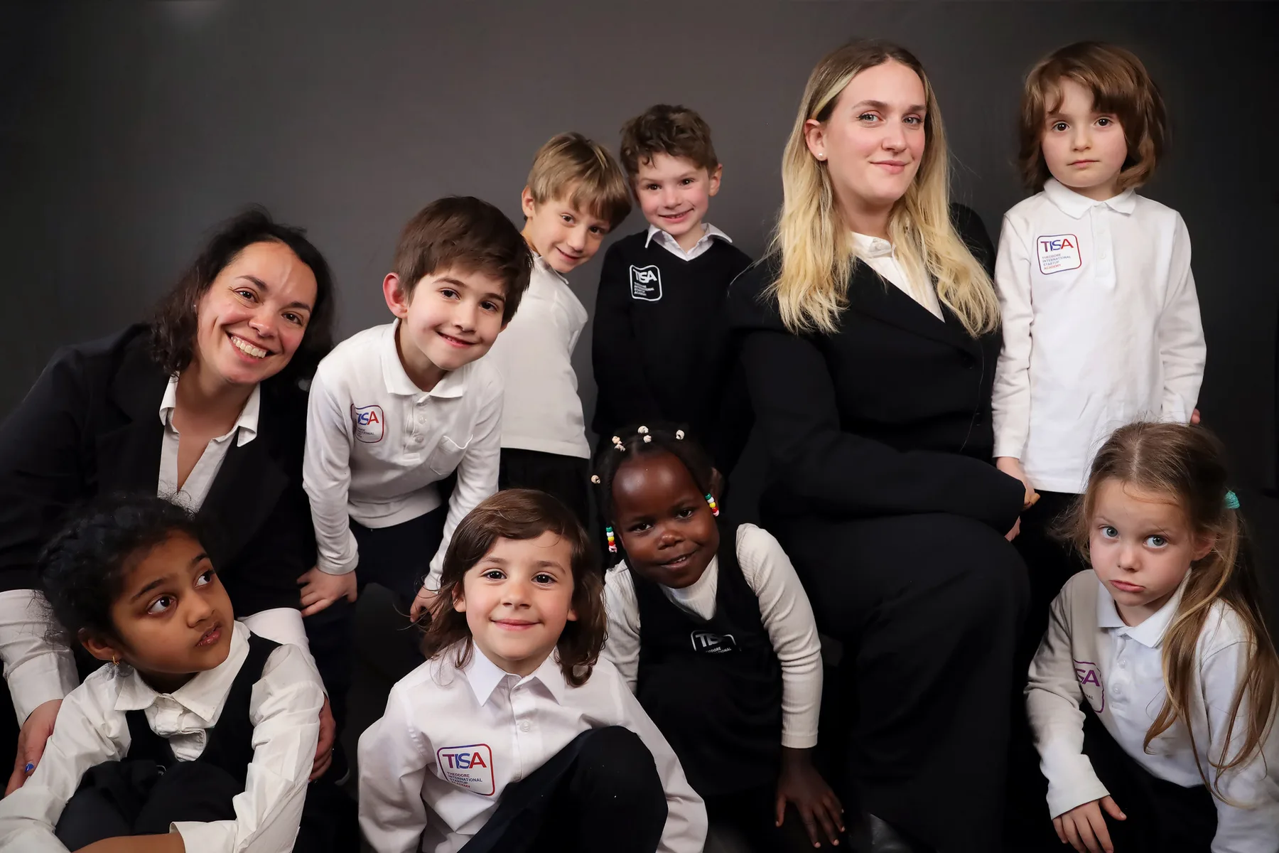 A large studio group photo of diverse TISA students of many ages together with two teachers