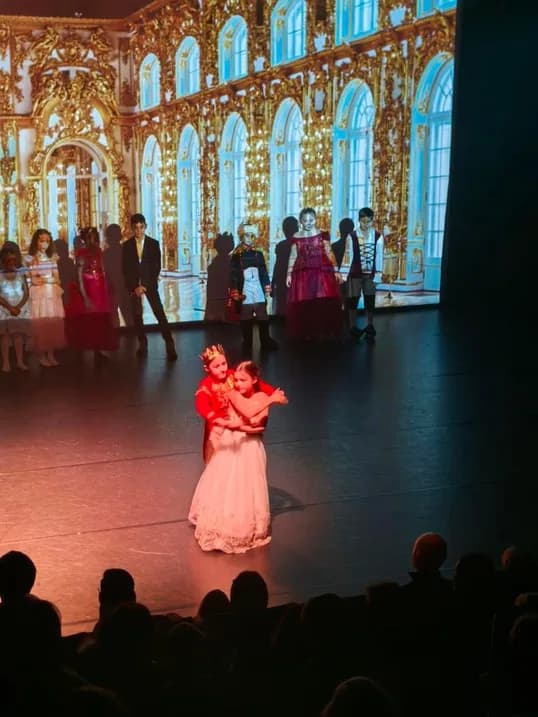 Two children dancing together on a golden-palace theatre stage at TISA